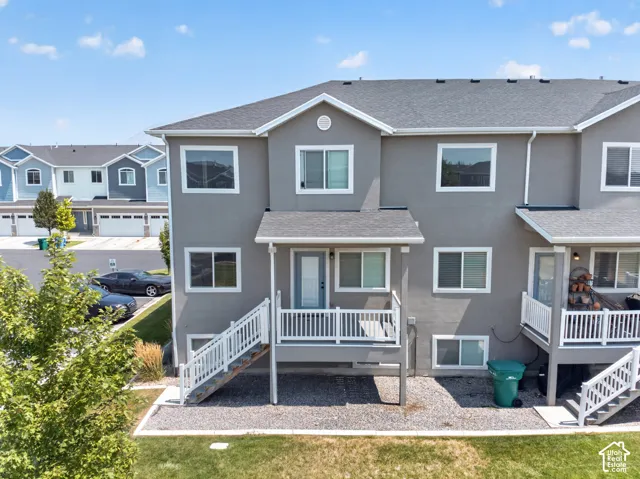 Rear exterior featuring a covered deck with white railings, a lower-level patio area, and a grey shingle roof