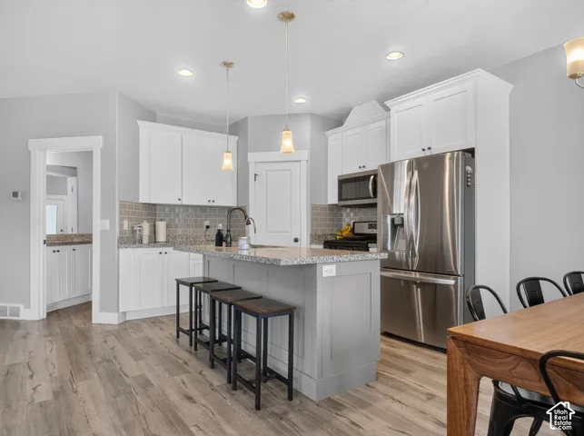 Modern kitchen featuring white shaker cabinetry, speckled countertops, stainless steel appliances, a tiled backsplash, and recessed lighting