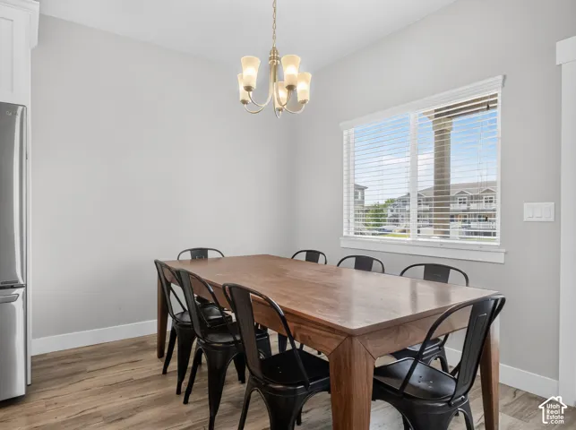Dining area featuring wood-finish flooring, a large window with white blinds, and a brass-tone chandelier