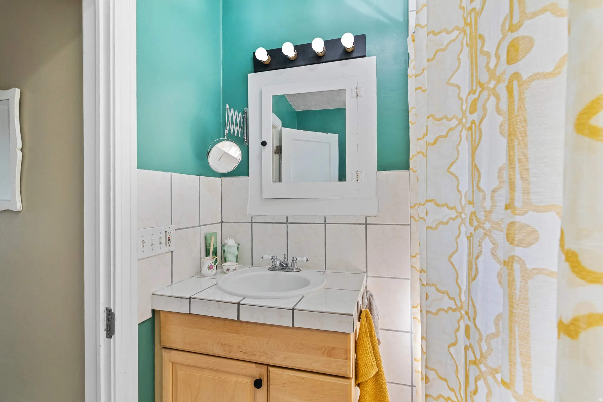 Bathroom vanity featuring a light wood-finish cabinet with black hardware, a recessed sink, and a tiled countertop