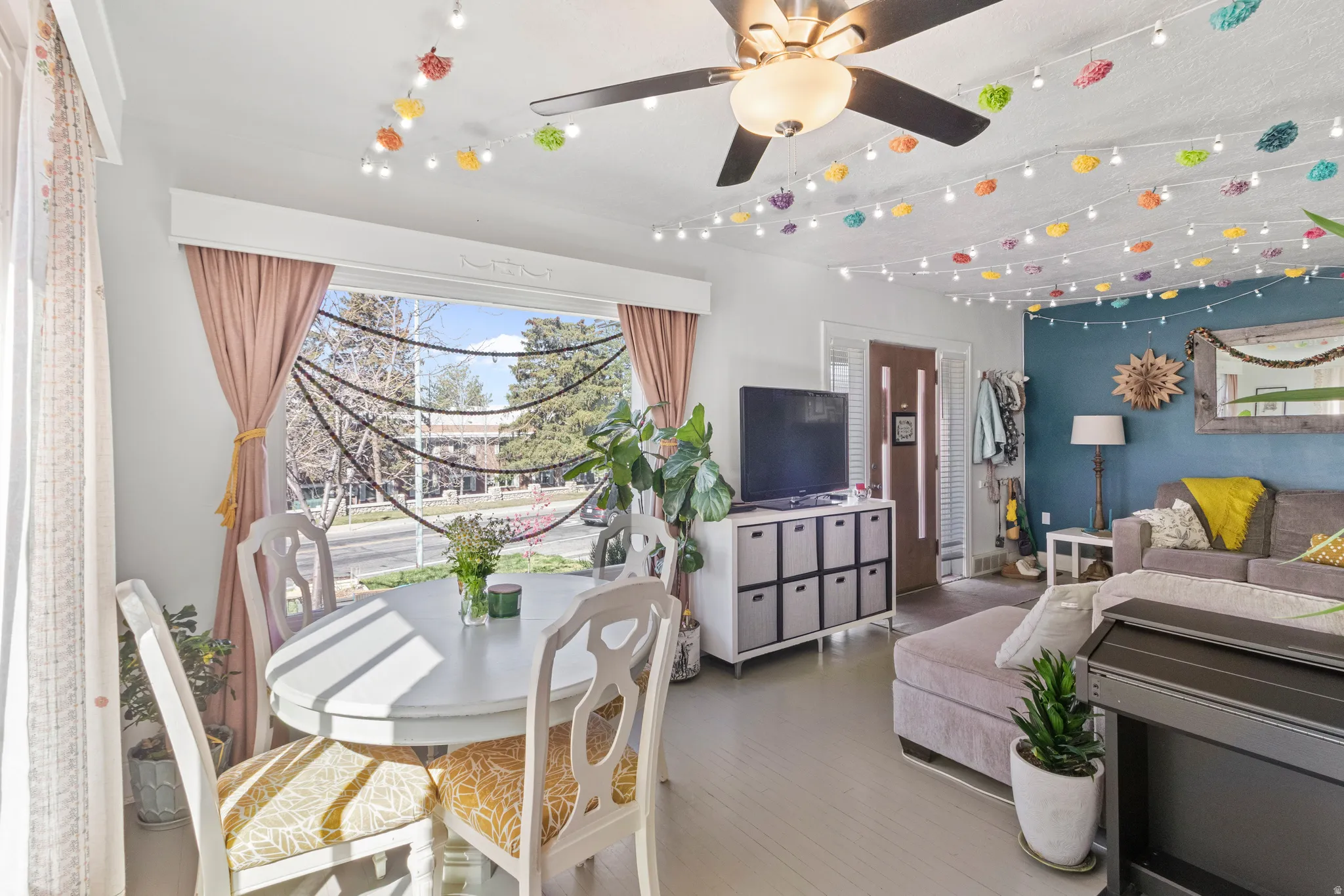 Open concept living area featuring a large picture window, light wood-finish flooring, and a ceiling fan