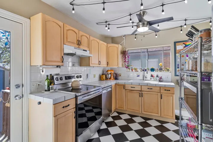 Kitchen featuring light wood-finish cabinetry, stainless steel appliances, a white tile backsplash, and a black and white checkered floor