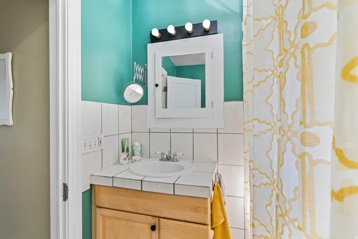 Bathroom vanity featuring a light wood-finish cabinet with black hardware, a recessed sink, and a tiled countertop