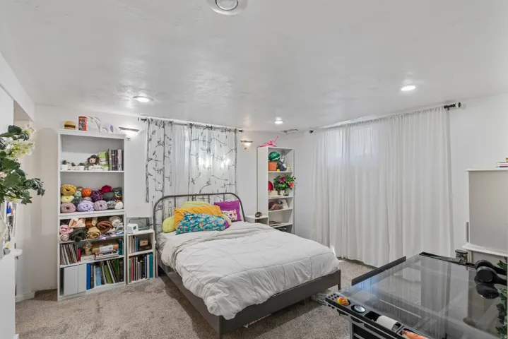 Spacious bedroom featuring recessed lighting and wall sconces, carpet flooring, a large window with sheer white curtains, and multiple built-in shelving units