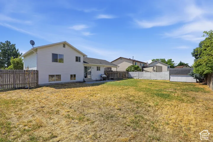 Expansive rear yard featuring a concrete patio, wood privacy fencing, and mature perimeter trees