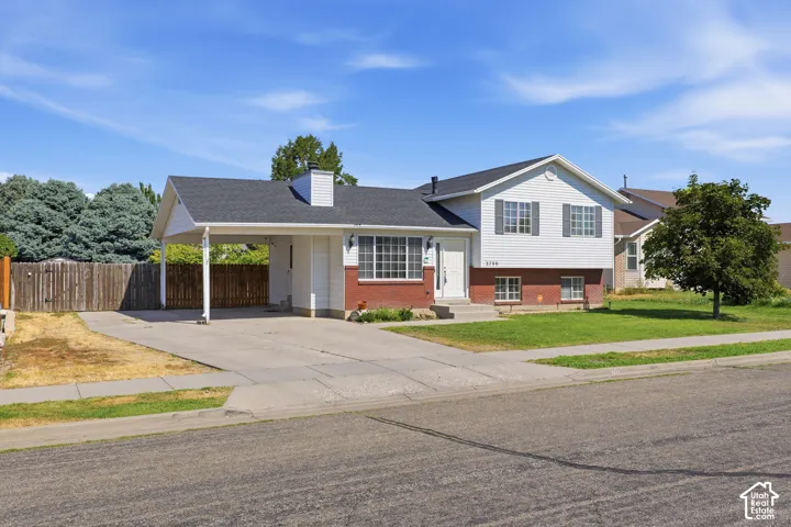 Split-level residence featuring a carport, a red brick facade with white siding, and a paved driveway