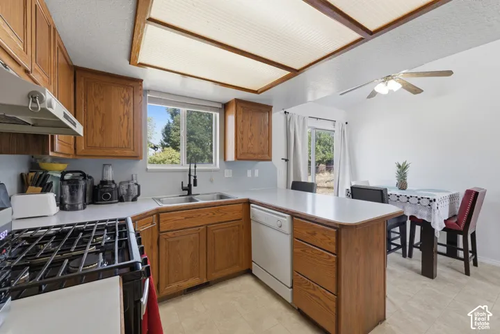 Spacious kitchen featuring warm wood cabinetry, a center island with drawers and counter seating, white countertops, gas range with black stovetop, stainless steel sink, and skylights providing natural illumination