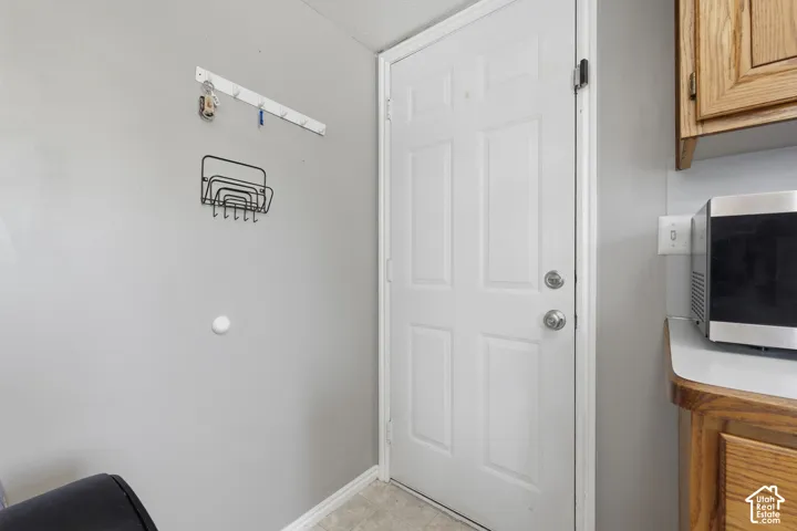 White paneled door with chrome hardware, light gray walls, and wood-finish cabinetry with a light-colored countertop