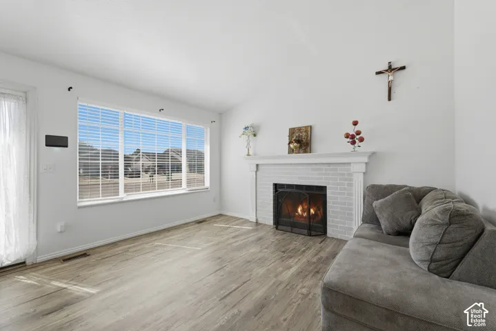 Bright living room showcasing large multi-pane windows with expansive natural light, wood-finish flooring throughout, and a fireplace with white mantel and surround