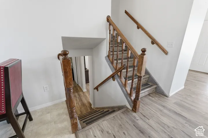 Elegant staircase featuring rich wood railings and balusters with turned newel posts, hardwood flooring throughout, and bright natural lighting from recessed ceiling details