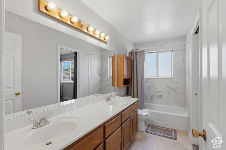 Spa-inspired primary bathroom featuring a dual-sink vanity with wood cabinetry, white quartz countertops, and polished brass hardware