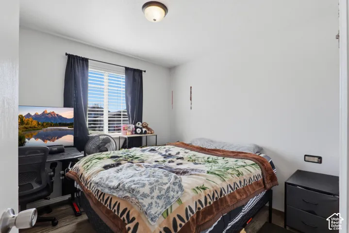 Comfortable bedroom featuring a bed with decorative bedding, dark wood-finish nightstand, desk workspace with task lighting, and large window with dark curtains framing mountain scenery