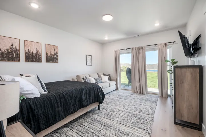 Spacious primary bedroom showcasing recessed ceiling lighting, sliding glass doors with thermal-efficient framing opening to expansive grounds, wood-finish flooring, and a neutral color palette with built-in cabinetry