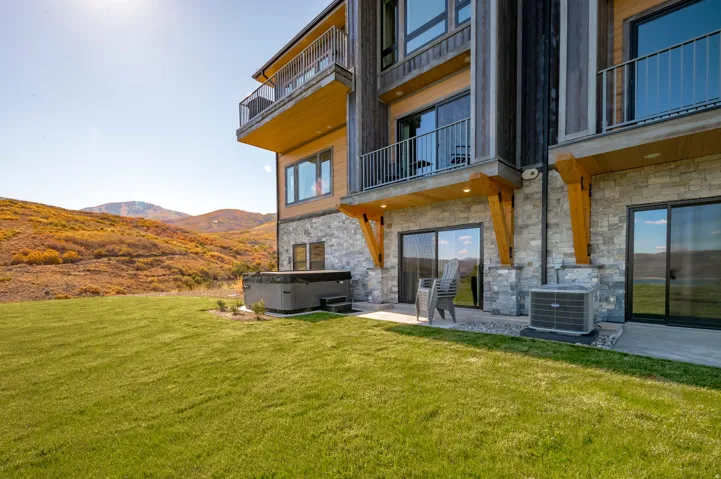 Stone facade with wood-finish siding, two private balconies with metal railings, and a ground-level patio with a hot tub