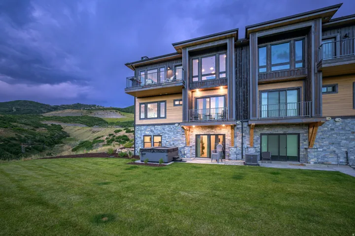Multi-level exterior with stone and wood siding, multiple balconies with metal railings, a ground-level patio, and an integrated hot tub