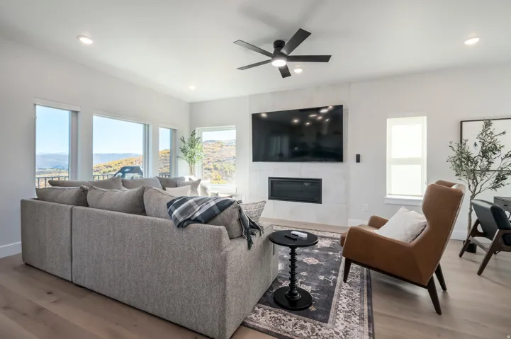 Expansive windows with mountain scenery, recessed lighting, wood-finish flooring, and a modern fireplace with a wall-mounted television