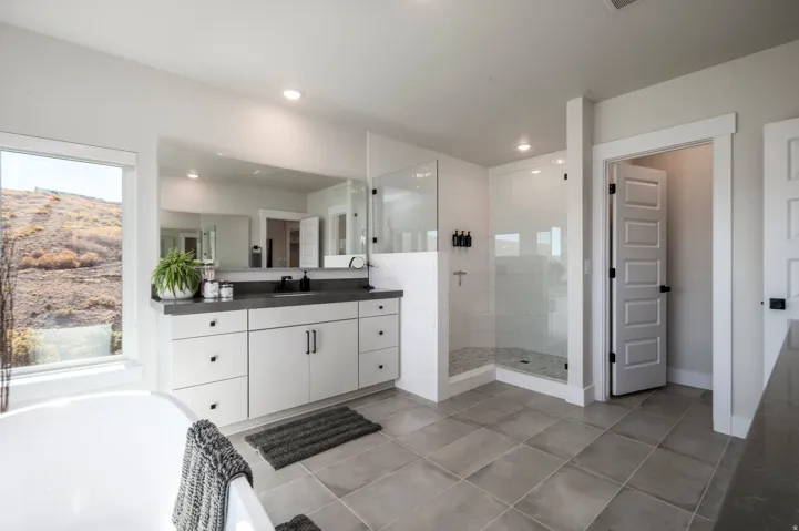 Spa-inspired primary bathroom featuring a dual-sink vanity with white cabinetry and black hardware, quartz countertop, large frameless glass-enclosed shower with tile surround, soaking tub, recessed lighting, and tile flooring throughout