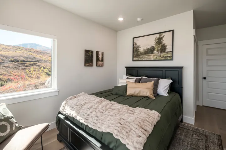 Bright bedroom with black upholstered headboard, wood-finish flooring, and large picture window with scenic mountain backdrop