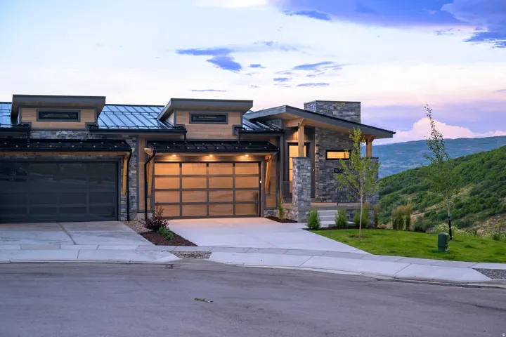 Modern architectural exterior featuring stone and wood-look siding, a metal roof, and an attached two-car garage with a translucent door