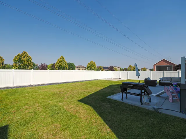 Expansive backyard featuring a green lawn, white privacy fencing, and a concrete patio