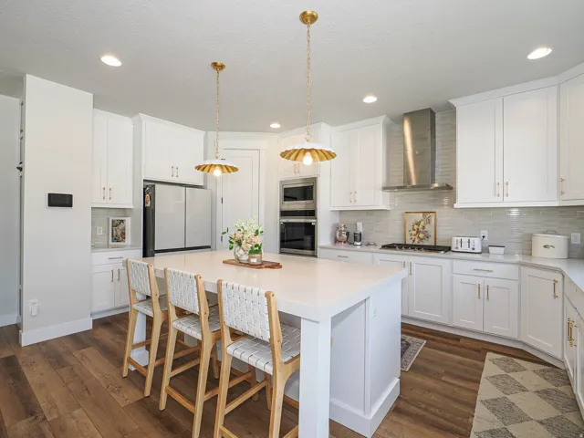 White cabinetry, stainless steel appliances, wood-finish flooring, recessed lighting, and a large central island with seating