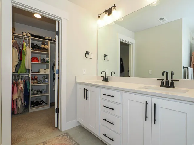 Double vanity with white cabinetry, matte black fixtures, and a large frameless mirror