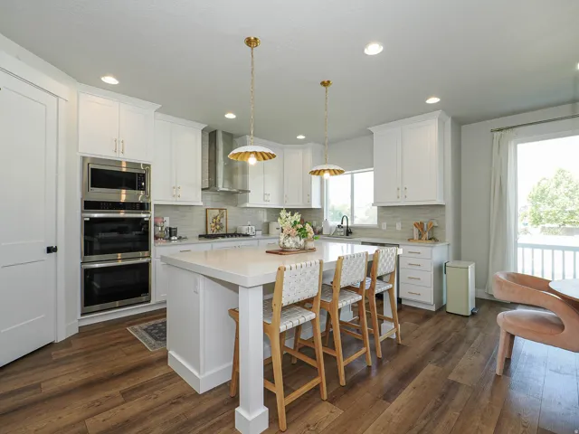 Kitchen featuring wood-finish flooring, white cabinetry, a center island with countertop seating, and stainless steel appliances including a built-in microwave and double oven