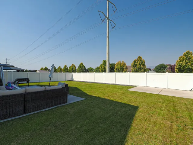 Expansive backyard featuring a manicured lawn, full white privacy fencing, and a concrete patio
