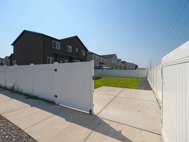 Paved driveway with a white privacy fence and gate, leading to a lawn area with dark gravel perimeter