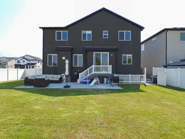 Expansive green lawn, a white privacy fence, a concrete patio, and a deck with white railings