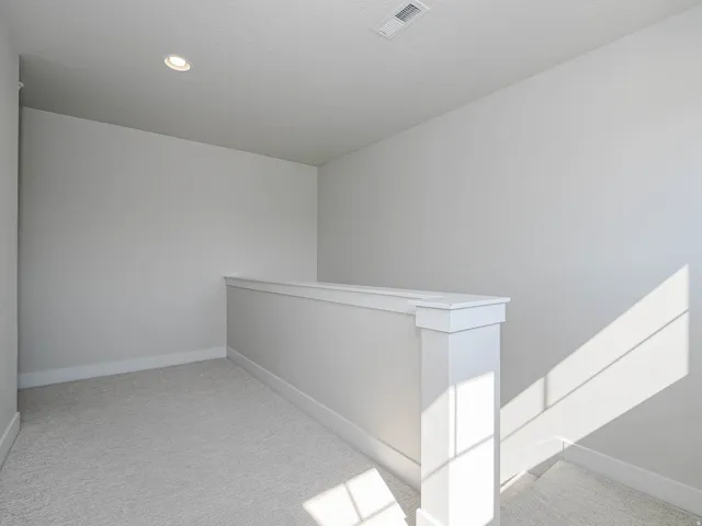 Carpeted landing with white balustrade and recessed ceiling light