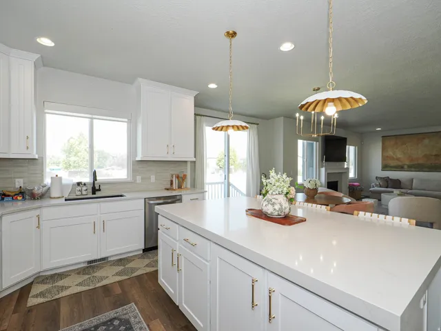 White cabinetry with gold-tone hardware, light-toned countertops, tile backsplash, stainless steel dishwasher, and wood-finish flooring