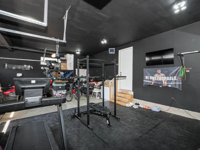 Finished garage space with dark walls and ceiling, equipped with overhead lighting and a white entry door