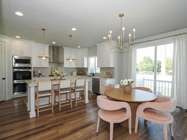 Open-concept kitchen and dining area featuring white cabinetry, stainless steel appliances, quartz countertops, a large center island with seating, wood-finish flooring, and abundant natural light from expansive glass doors and windows