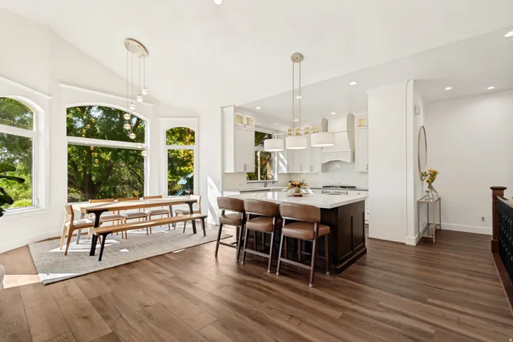 Open-concept living area with wood-finish flooring, a kitchen island with seating, white cabinetry, and large arched windows