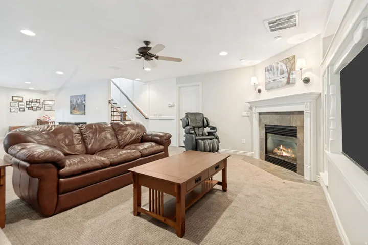Spacious living room featuring a gas fireplace with white surround and mantel, recessed ceiling lighting, ceiling fan, and neutral wood-finish flooring throughout