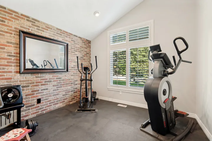 Vaulted ceiling with an exposed brick accent wall, large framed mirror, and plantation-shutter windows