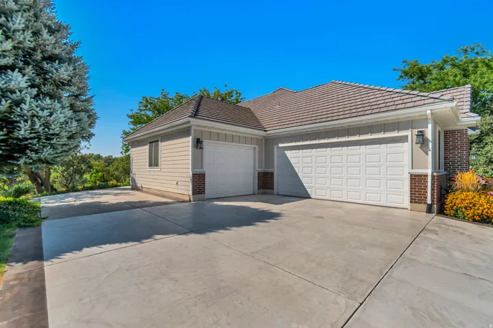 Exterior featuring tan siding, brick accents, concrete driveway, and a multi-car garage with white panel doors