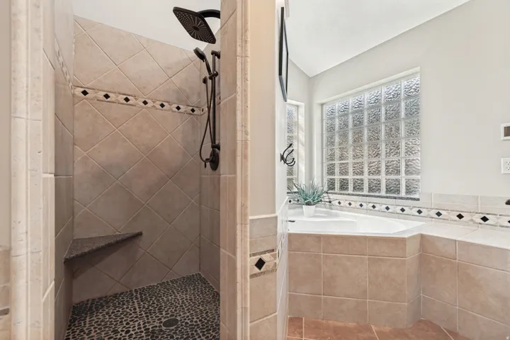 Spa-inspired primary bathroom featuring a custom walk-in shower with diagonal tile layout, rainfall showerhead, and pebble stone flooring