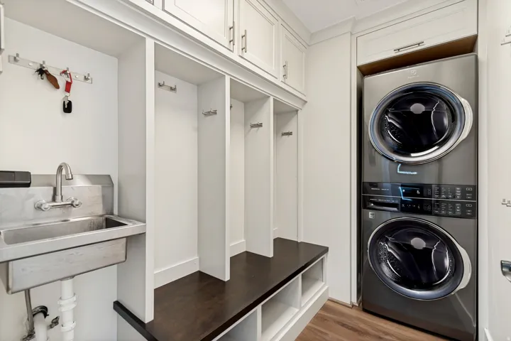 Built-in cabinetry with brushed nickel hardware, stainless steel utility sink, built-in bench seating with storage, and wood-finish flooring