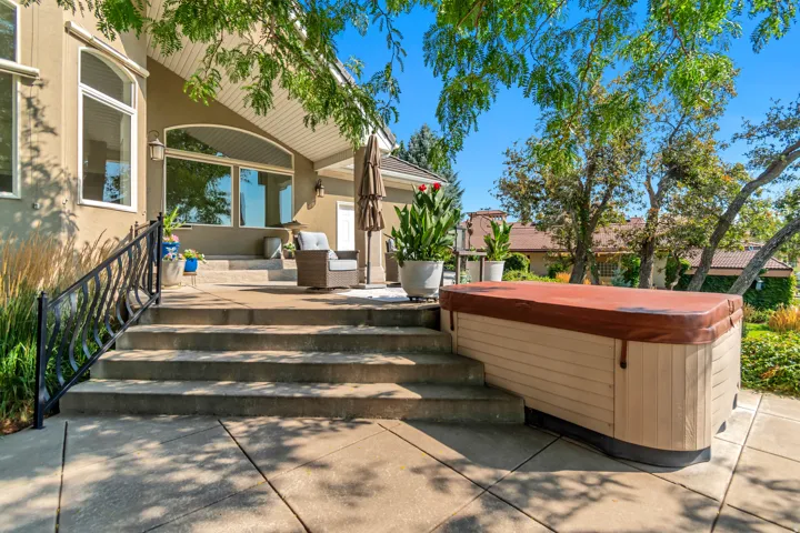 Concrete patio with a hot tub, stucco exterior, and black wrought iron railing
