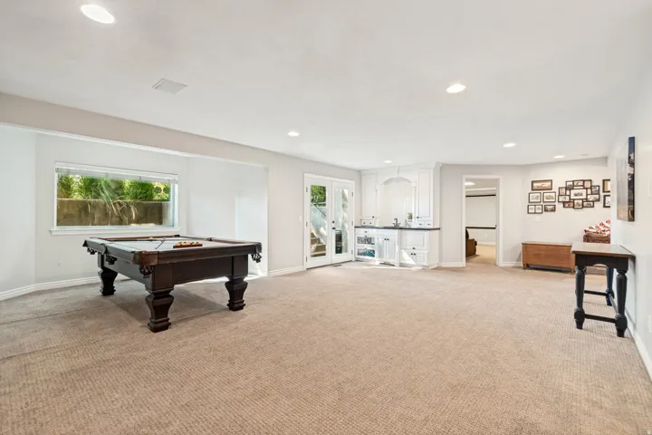 Expansive carpeted room featuring a built-in wet bar with white cabinetry, a sink, and french doors