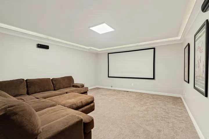 Dedicated media room featuring a built-in projection screen, recessed ceiling lighting, and neutral carpet flooring