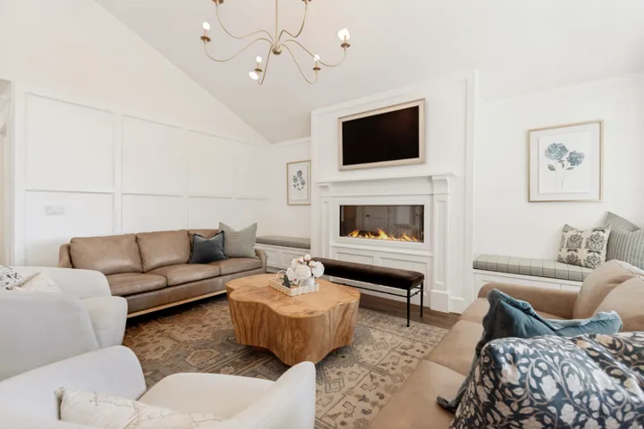 Sophisticated living room showcasing a linear gas fireplace with integrated shelving, vaulted ceiling with modern pendant lighting, plush seating arrangements, and a natural wood-finish accent table