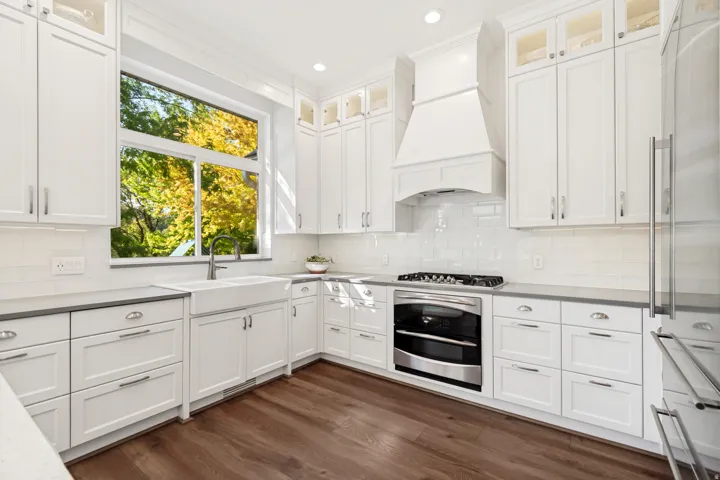 Chef's kitchen featuring white shaker cabinetry with stainless steel hardware, quartz countertops, a gas range with black stove and white hood, and stainless steel refrigerator