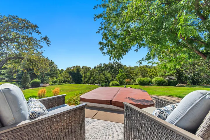 Expansive backyard featuring a hot tub, stone patio, and mature trees