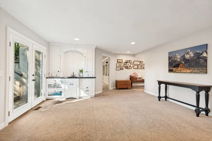 Built-in wet bar with white cabinetry and dark countertop, double French doors, recessed lighting, and neutral carpet