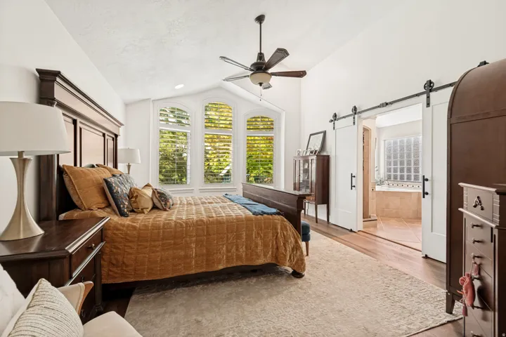 Vaulted ceiling with a ceiling fan, hardwood flooring, and white plantation shutters
