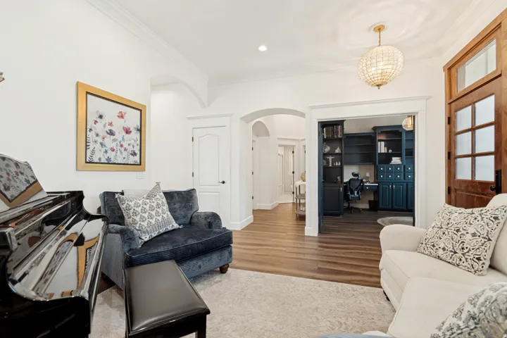 Elegant living space featuring hardwood flooring, a black upholstered armchair, cream-toned seating, arched doorways with white trim, recessed ceiling lighting, and a gold-framed artwork