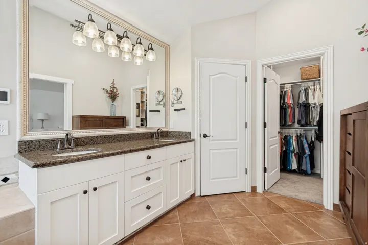 Dual vanity with granite countertop, white cabinetry, undermount sinks, and a framed mirror